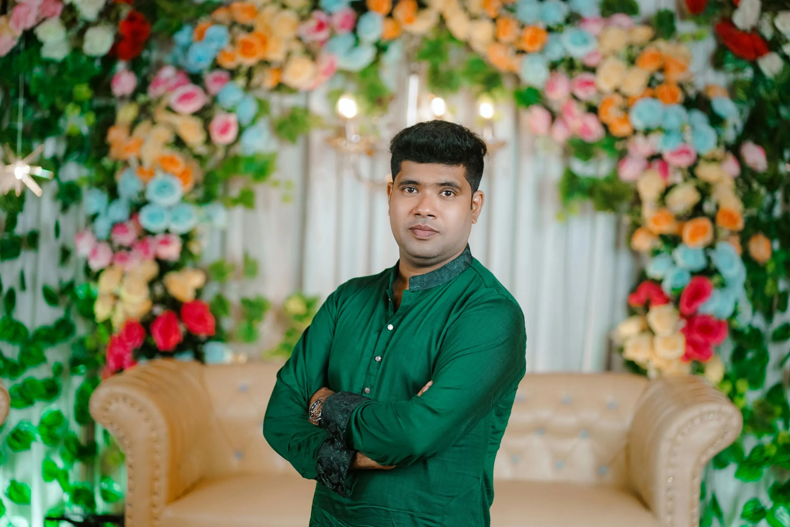 Elegant portrait of a man in traditional attire at a Bengali wedding, surrounded by colorful floral decor.