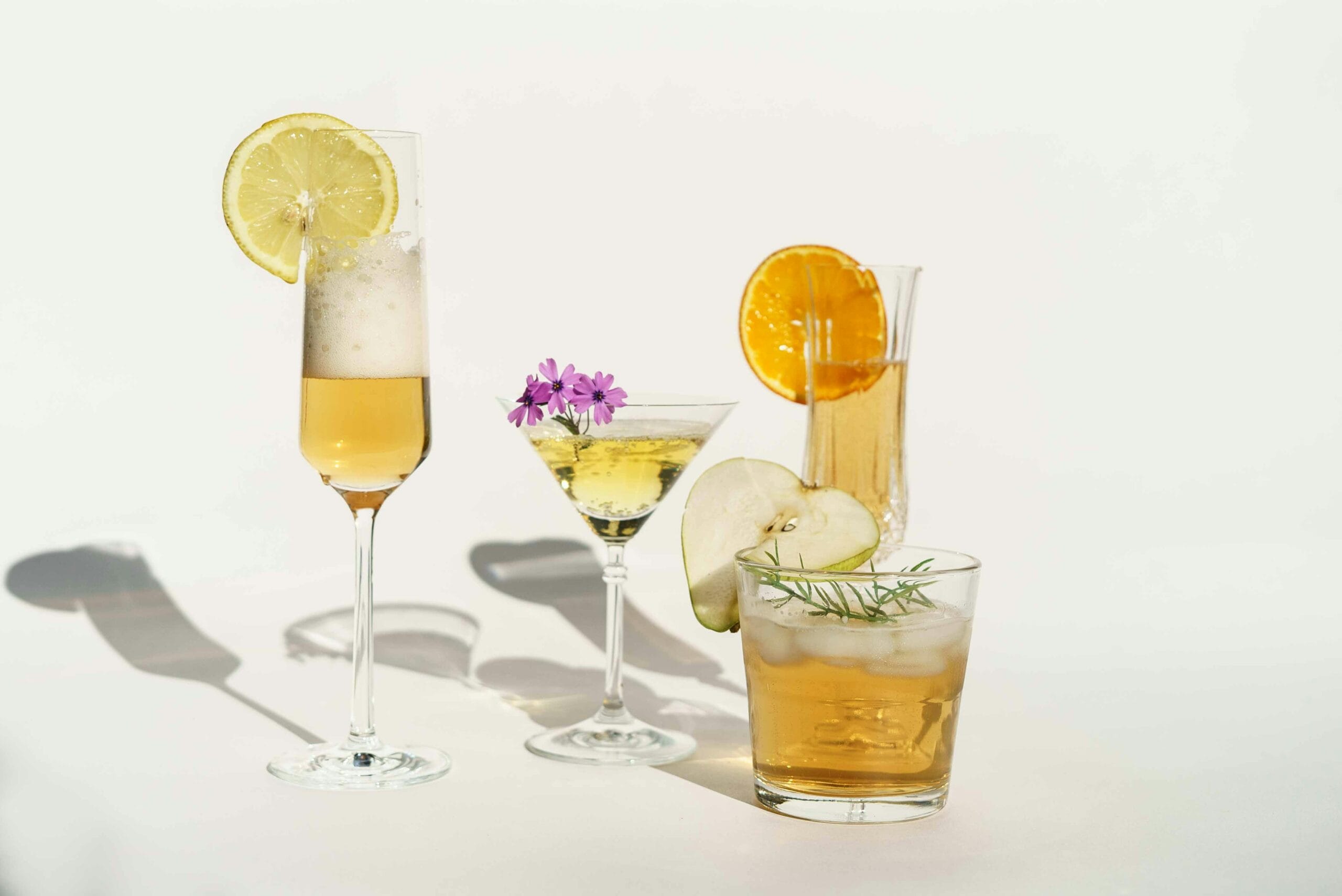 A stylish collection of cocktails garnished with fruits and flowers, perfectly lit on a white background.