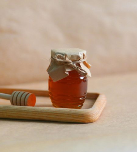 A homemade jar of honey with a rustic wrapping on a wooden tray, showcasing natural sweetness.